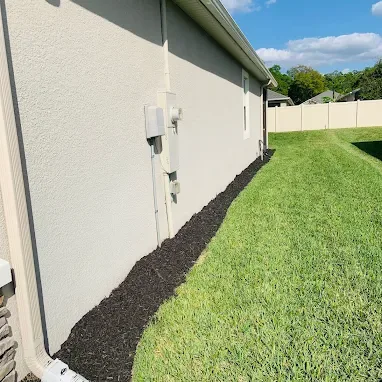 Fresh black mulch along a side wall with a neatly mowed lawn