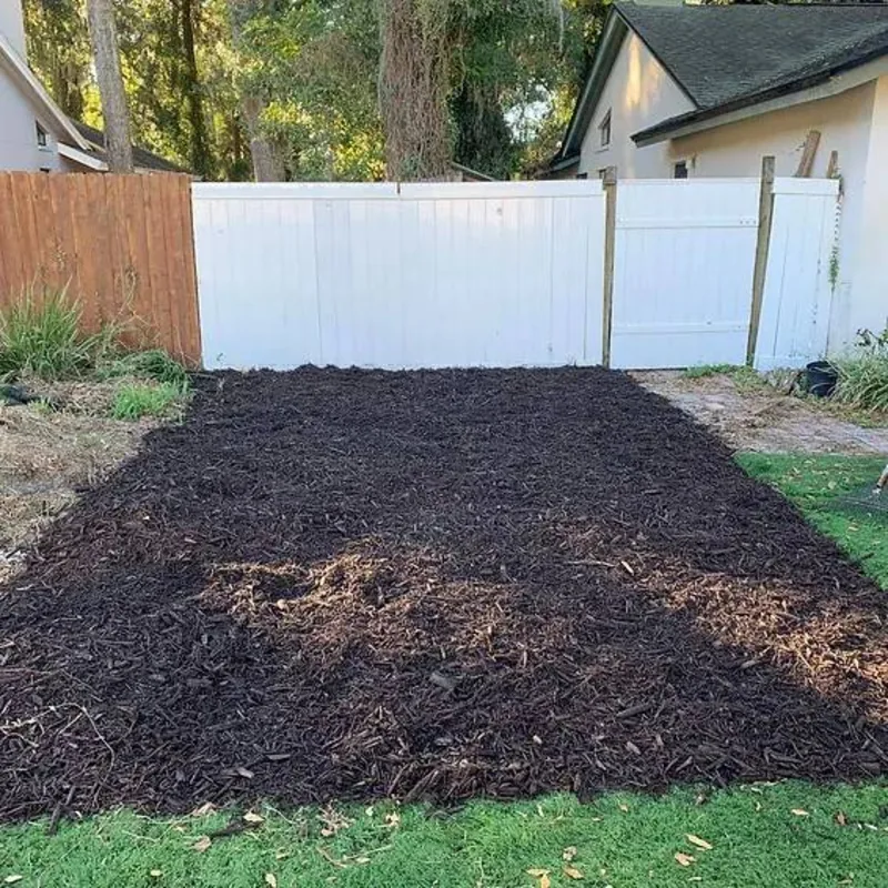 Large back garden bed freshly topped with dark mulch along a fence line